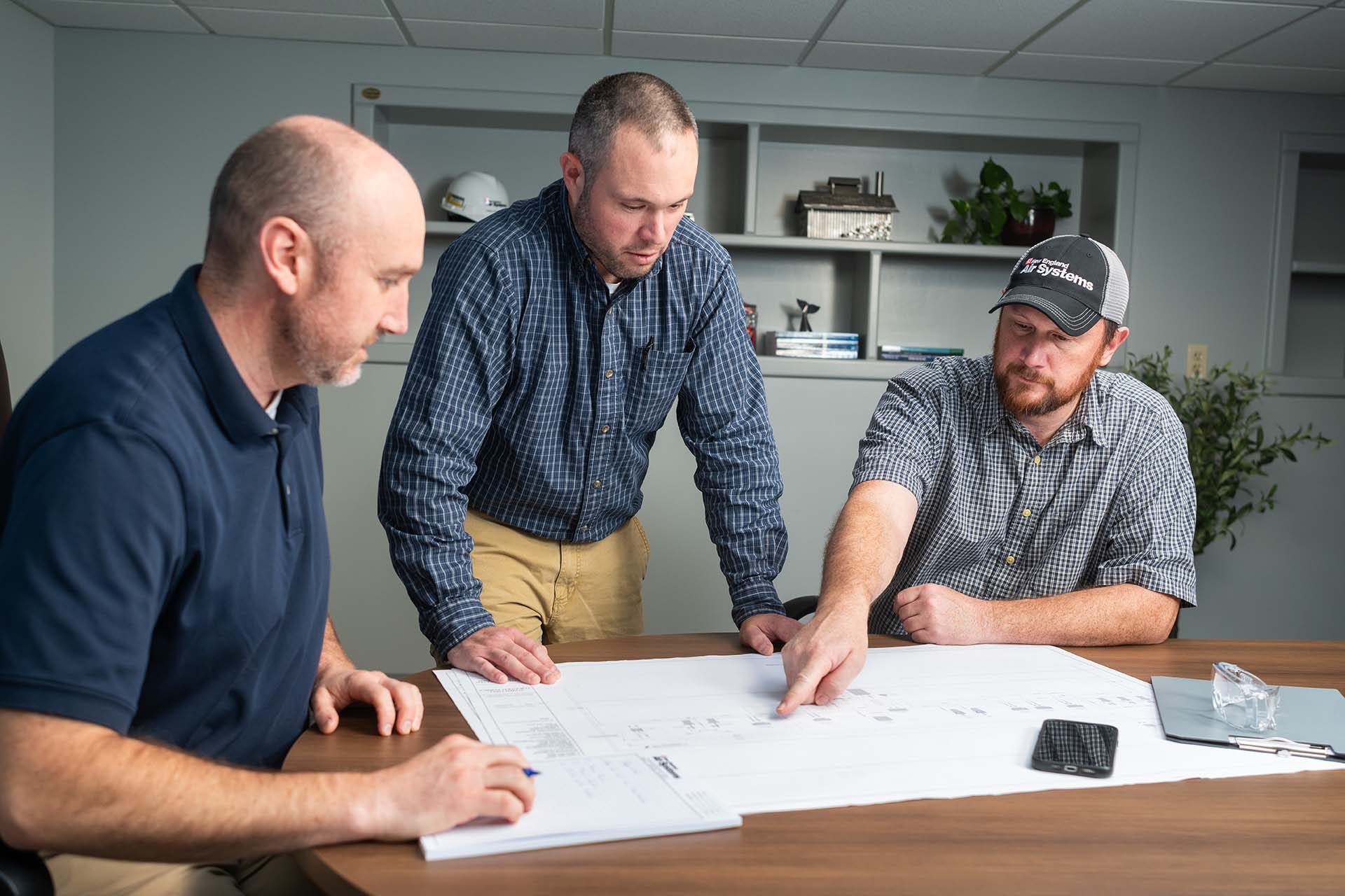 3 employees at table discussing HVAC and plumbing design plan