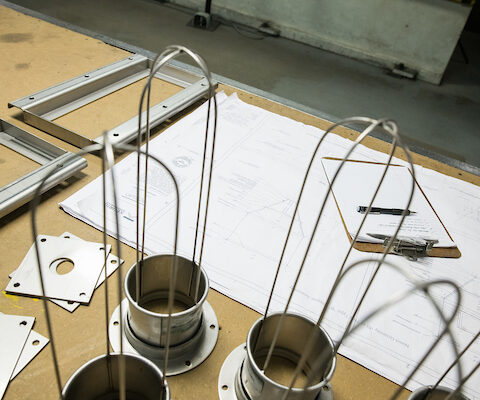 table with blueprint plans for Keurig coffee bean hoppers, a clipboard and parts