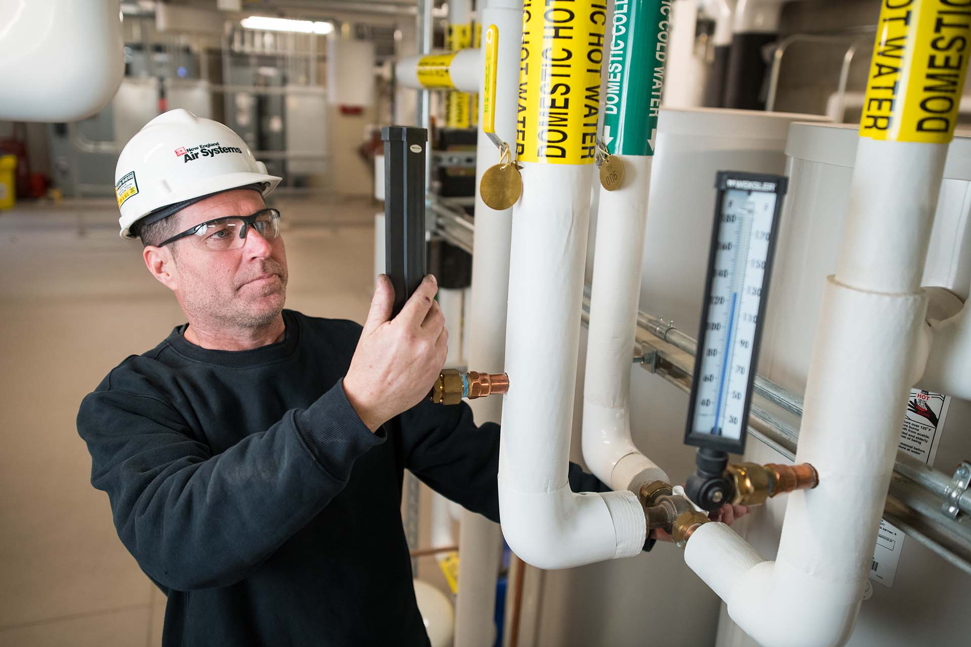 NE Air employee wearing hard hat performing service on HVAC plumbing