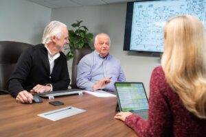 3 employees talking at meeting with a design plan on a TV screen